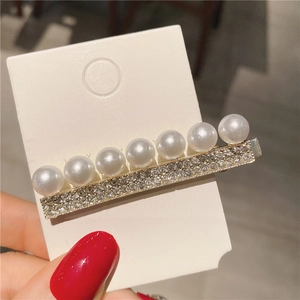 Gros plan détaillé d'une barrette longue avec sept perles blanches et des strass étincelants