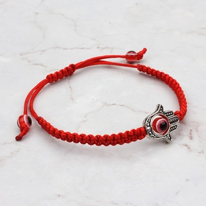 Détail d'un bracelet tressé rouge avec breloque main de Hamsa et perles mauvais œil