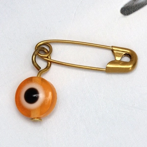 Detalle del broche de mal de ojo con alfiler dorado y colgante de cuenta naranja