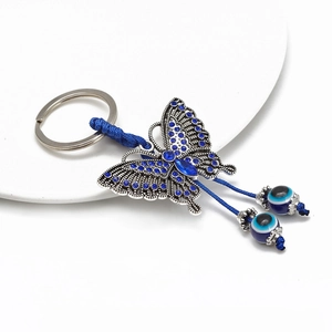 Detailed close-up of blue butterfly keychain with evil eye beads on white ceramic tray