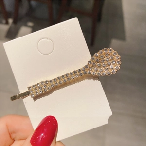Détail d'une pince à cheveux dorée en forme de cuillère avec strass sur carte de présentation