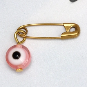 Primer plano de un broche de imperdible dorado con colgante de cuenta de ojo turco rosa