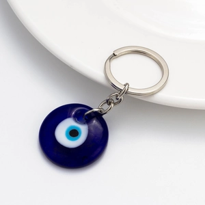 Classic blue glass Evil Eye keychain with silver metal ring on a white ceramic plate