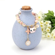 Detailed view of beaded bracelet with pink matte beads and cute floral charms on blue vase