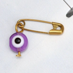 Detalle de broche de imperdible dorado con cuenta de ojo turco púrpura en tela blanca