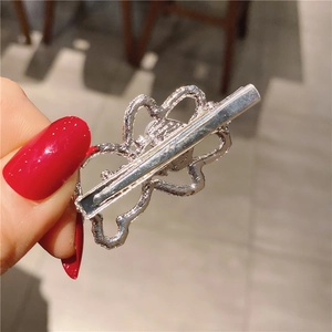 Détail d'une pince à cheveux argentée ajourée avec motif à vagues et clip à ressort en métal