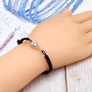 Détail du bracelet tressé noir avec breloque œil porte-bonheur dorée et nœud coulissant