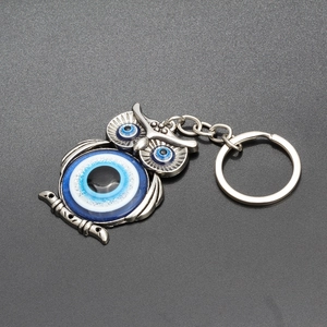 Silver owl keychain with blue evil eye charms on a dark textured background