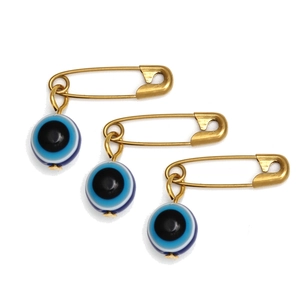 Detalle de tres imperdibles de ojo turco dorados con cuentas azules sobre fondo blanco