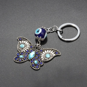 Detail showing butterfly keychain with evil eye bead and blue crystals on grey surface