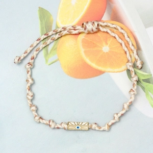 Detailed view of woven Evil Eye bracelet with a gold metal plate on a summer theme backdrop