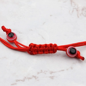 Bracelet tressé rouge avec œil maléfique et nœud réglable sur fond marbre