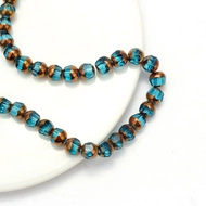 Macro detail of faceted teal beads and bronze metal spacers on white porcelain