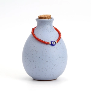 Deep red beaded garnet bracelet with lucky blue evil eye charm on ceramic vase