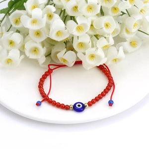 Detail of red beaded bracelet with blue evil eye charm on a white ceramic flower tray