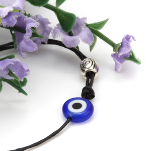 Macro-opname van blauwe evil eye glaskraal en zilveren filigraanbedel op een zwart koord
