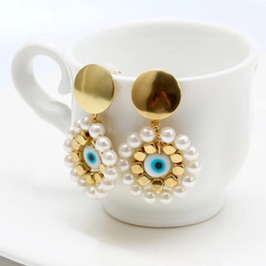 Detail of ethnic evil eye earrings with white pearls and gold accents on a ceramic cup
