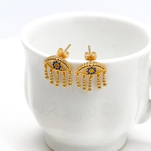 Detail of golden Evil Eye tassel earrings with blue zircon dangling from a white ceramic cup