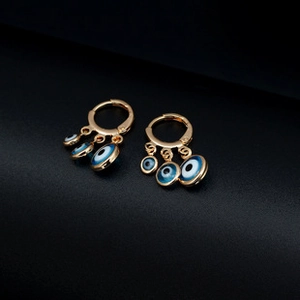 Close-up of golden hoop earrings featuring three tiered blue evil eye enamel pendants