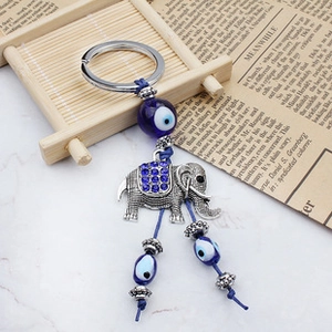 Detail of silver elephant keychain with blue evil eye beads on a rustic bamboo tray