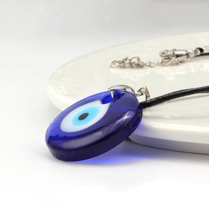 Classic blue glass Evil Eye pendant necklace on white ceramic tray with black cord strap