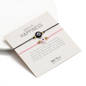 Detail der gewebten Evil Eye Armbänder in Schwarz und Rosa auf einer Wunschkarte