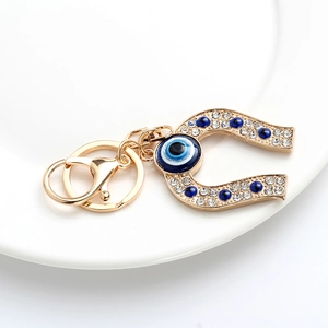 Golden horseshoe keychain with blue evil eye beads and rhinestones on white tray