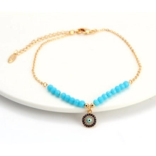 Detail of a golden Evil Eye bracelet with blue beads, lobster clasp and extension chain