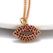 Macro shot of gold-plated lip pendant necklace with red cubic zirconia stones on white ceramic