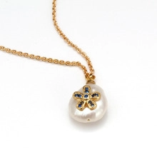 Macro view of Baroque pearl pendant with blue floral detail on gold chain necklace