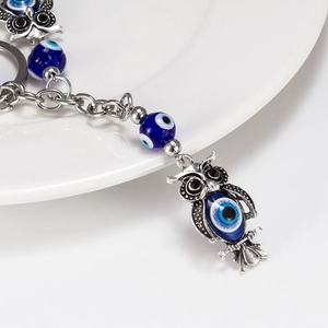 Close-up of vintage silver owl keychain with blue evil eye beads and metal ring