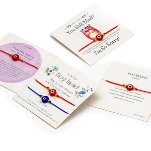 Detail von handgewebten Evil Eye Armbändern in Rot und Blau auf Geschenkkarten für Freunde