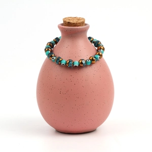 Detailed shot of Evil Eye beaded bracelet with turquoise and gold beads on pink vase