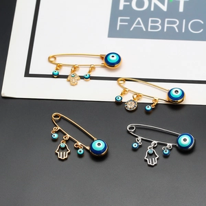 Detailed close-up of Evil Eye and Hamsa Hand charms on gold and silver safety pin brooches