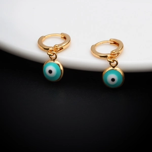 Detailed close-up of golden evil eye huggie hoop earrings with blue enamel charms on white ceramic