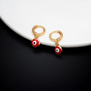 Golden hoop earrings with red evil eye charms displayed on a white ceramic plate