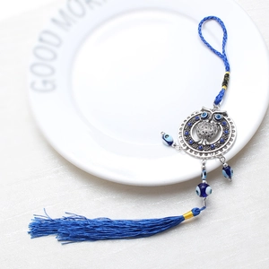 Detail of owl and blue evil eye pendant with tassel on white ceramic plate