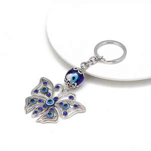 Macro shot of silver butterfly evil eye keychain with blue rhinestones on white plate