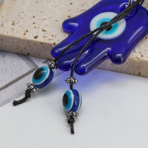 Detail der Hamsa-Hand aus blauem Glas und Evil Eye Anhänger mit geflochtenem Seil und Perlen