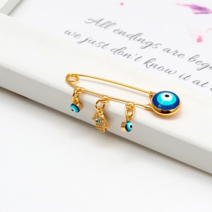 Macro shot of gold safety pin brooch with blue evil eye and Hamsa hand charms