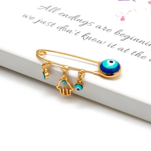 Close-up of golden safety pin brooch with Hamsa Hand and blue Evil Eye charms