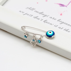 Close-up detail of silver Hamsa Hand and blue Evil Eye charms on a safety pin brooch