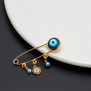 Close-up of golden Evil Eye safety pin brooch with blue enamel and pave stone charms