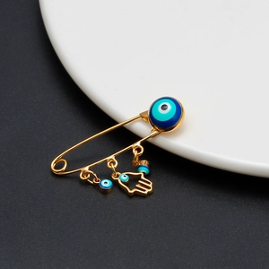 Close-up of golden Evil Eye safety pin brooch with Hamsa Hand and blue enamel charms