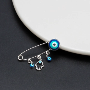 Macro detail of silver evil eye safety pin brooch with hamsa hand charms and blue beads