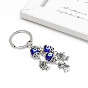 Detail of evil eye keychain with blue beads and palm tree pendants on white background