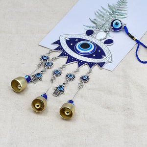 Blue Evil Eye wall hanging with Hamsa hand charms and golden bells on beige linen