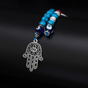 Detailed view of silver Hamsa Hand pendant with blue Evil Eye beads on a black base