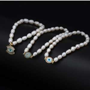 Détail de bracelets en perles d'eau douce avec charms œil maléfique dorés sur fond noir