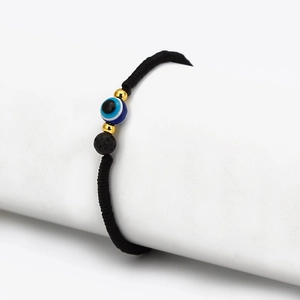 Detail of hand-woven cord bracelet featuring an Evil Eye bead and lava stone charm